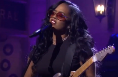 H.E.R tocando guitarra e cantando no microfone (Reprodução)